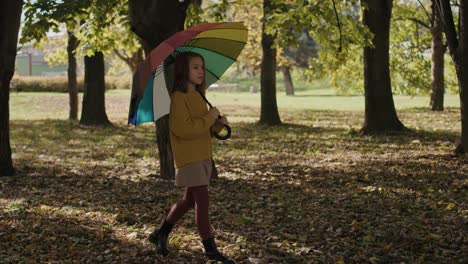 caucasian girl walking across the park with colorful umbrella.