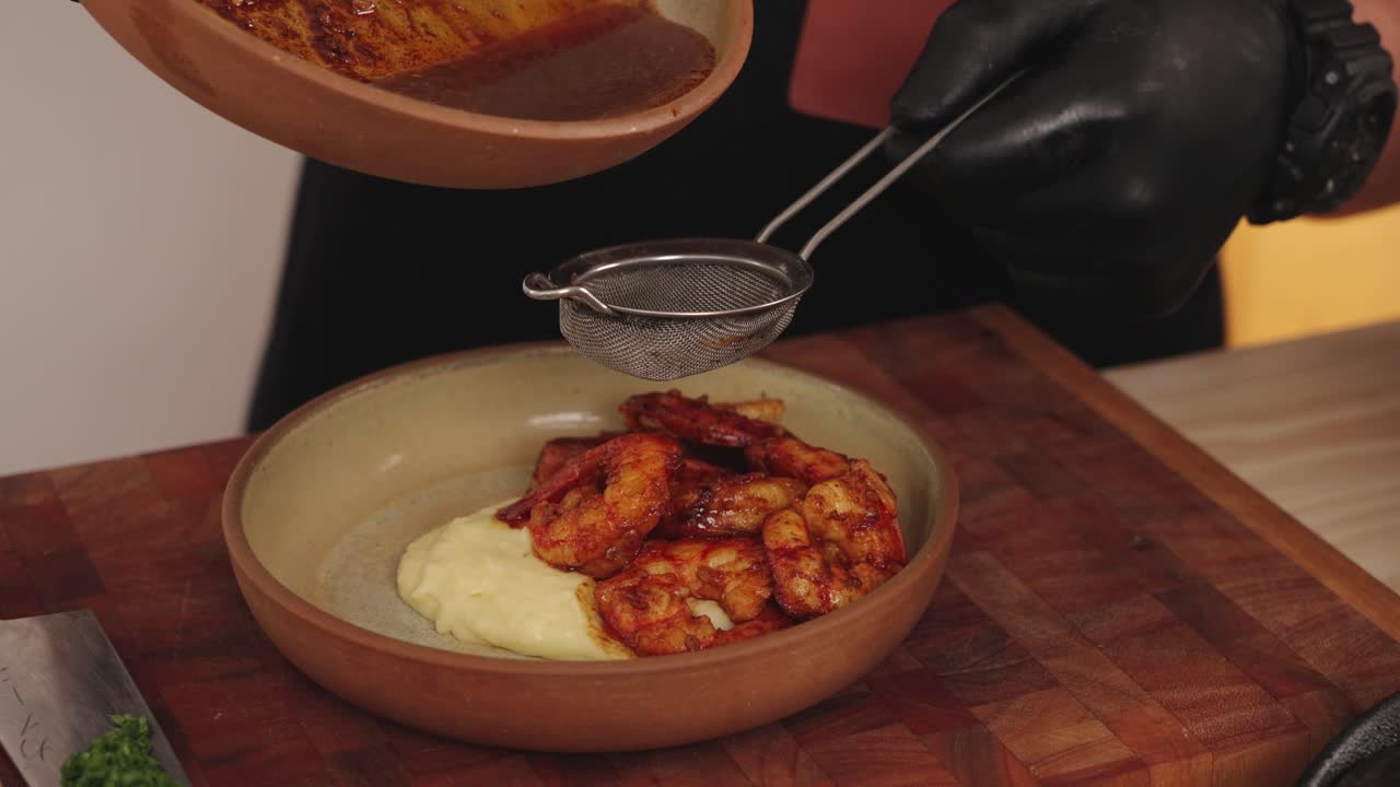 chef sin rostro usando un colador de alimentos colando la salsa, agregando el líquido a un plato gourmet de mariscos, camarones con plato de puré de papas