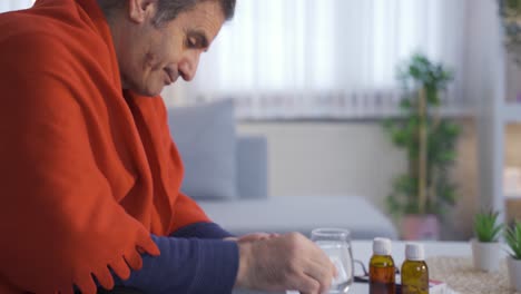 Sick-mature-man-sitting-on-sofa-at-home-and-drinking-his-medicine.