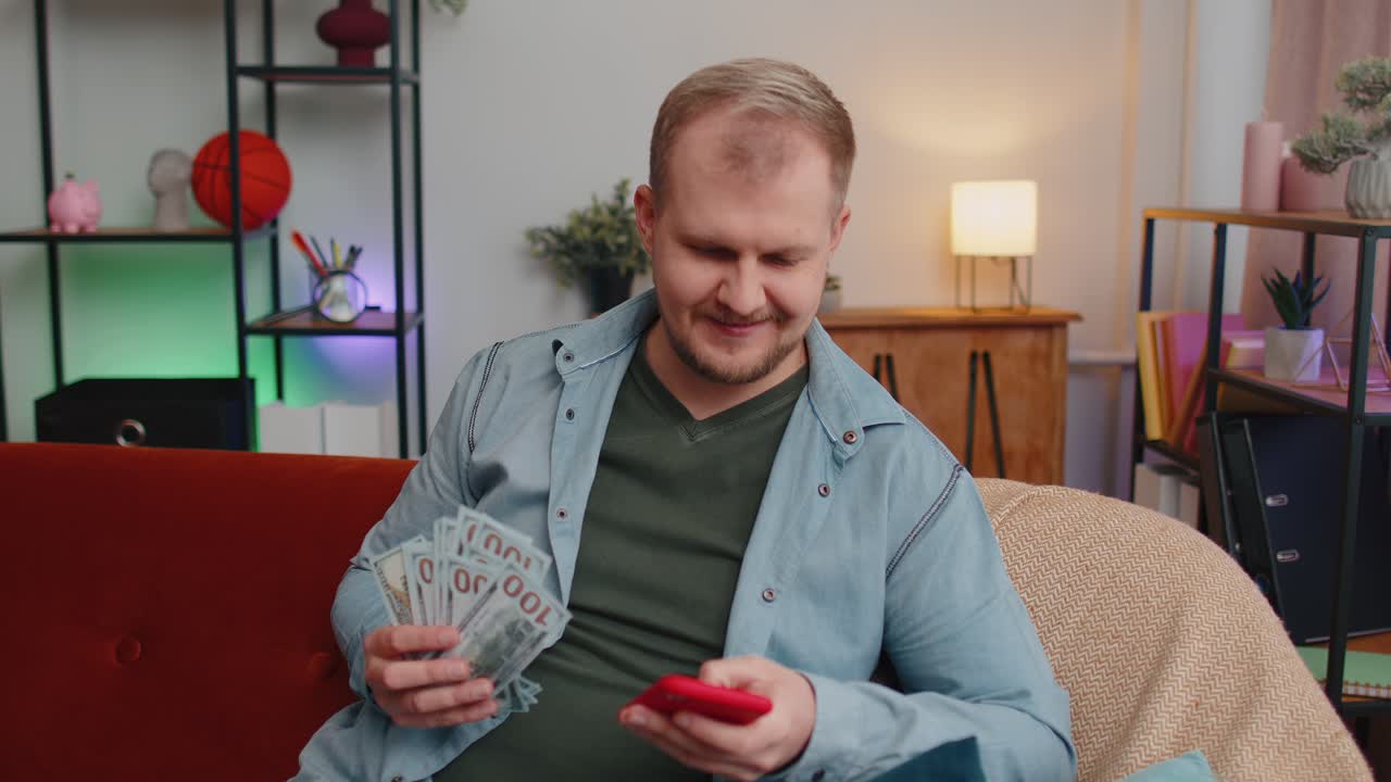 joven feliz sonriente contando dinero en efectivo y usar teléfono móvil calcular facturas domésticas en casa