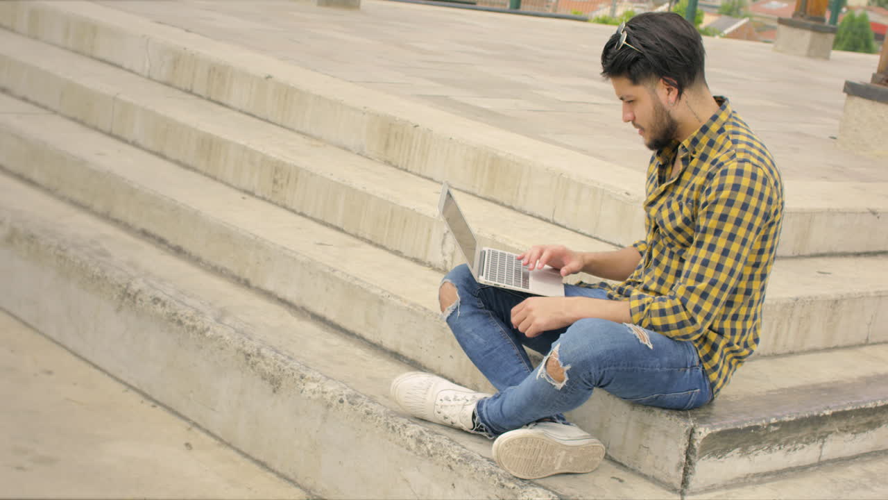 Uomo attraente seduto sulle scale che usa un laptop all'aperto.