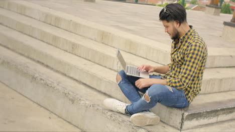 Hombre-Guapo-Sentado-En-Las-Escaleras-Usando-Una-Computadora-Portátil-Al-Aire-Libre