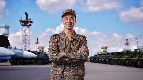 아시아인 군인이 미소 짓고 군 캠프에 서서 팔을 고 있다
