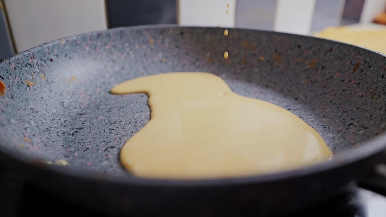 Smooth yellow pancake batter dripping slowly into hot frying pan, close up view