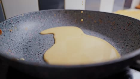 smooth yellow pancake batter dripping slowly into hot frying pan, close up view