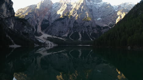 Drone-shot-tilting-over-boats-on-mirroring-lake-Pragser-Wildsee,-in-sunny-Dolomites,-Italy