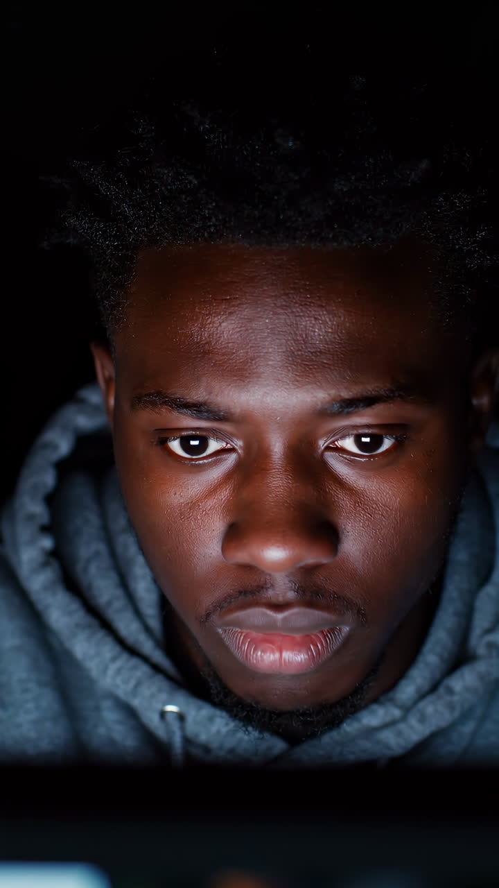 Young Black Man In Hoodie Focused On Laptop Screen Glow, Latenight Remote Coding Session, Intense