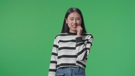 asian woman having toothache while standing in front of green screen background