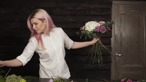 young woman determines the design of a bouquet and composition holding a set of flowers. next to the table is a variety of flowers for work