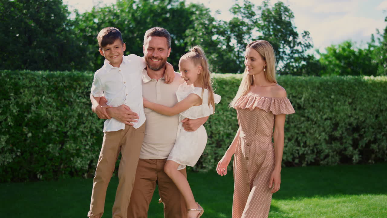 아버지는 딸과 아들을 손에 들고 있다. 부모와 아이들은 카메라에 포즈를 취하고 있다.