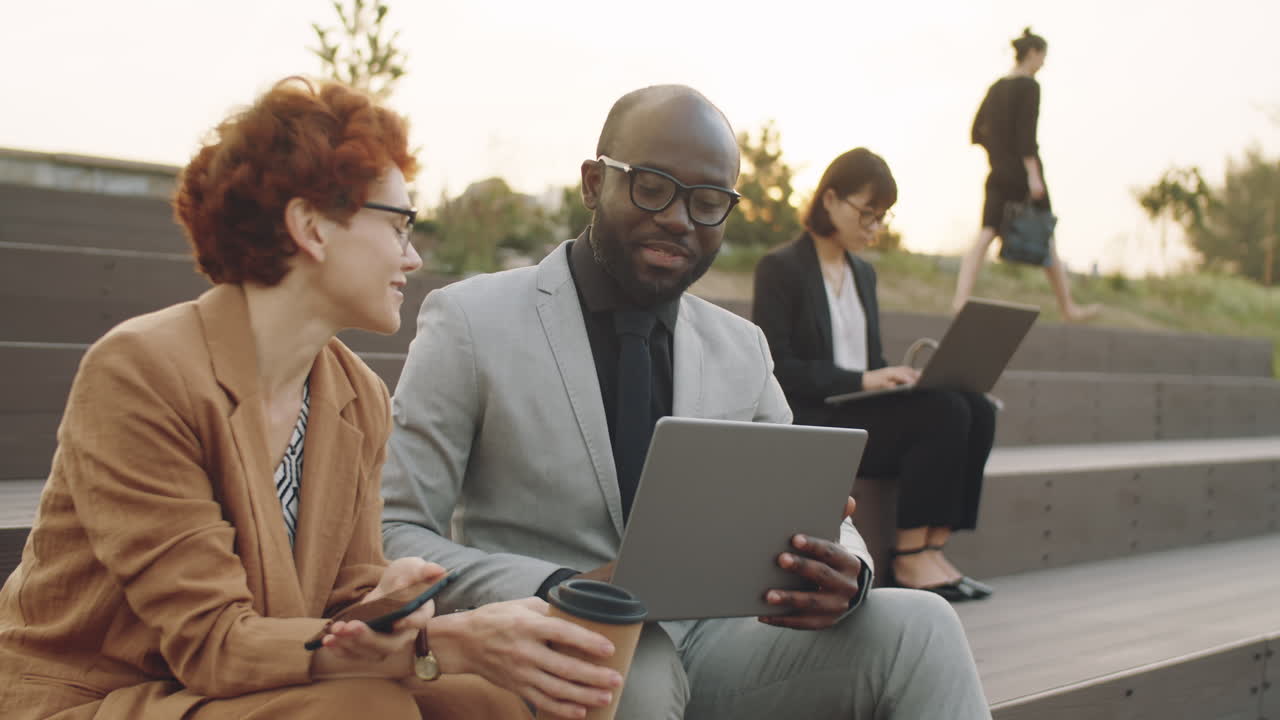 Multiethnic Man and Woman Working on Laptop and Speaking Outdoors