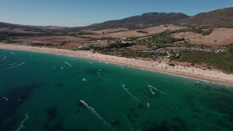 dolly-left-aerial-video-of-kitesurfers-practicing-and-having-fun-on-sunny-day-at-Tarifa-Beach,-Cadiz,-spain