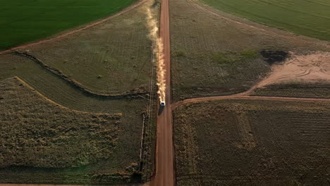 Aerial-shot-of-car-driving-on-dirt-road-in-near-pivots-with-green-farm-growth-in-Willcox,-Arizona,-wide-downward-angle-drone-shot