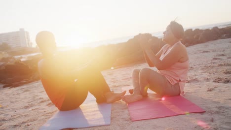 happy senior african american couple doing yoga, meditating at beach, slow motion