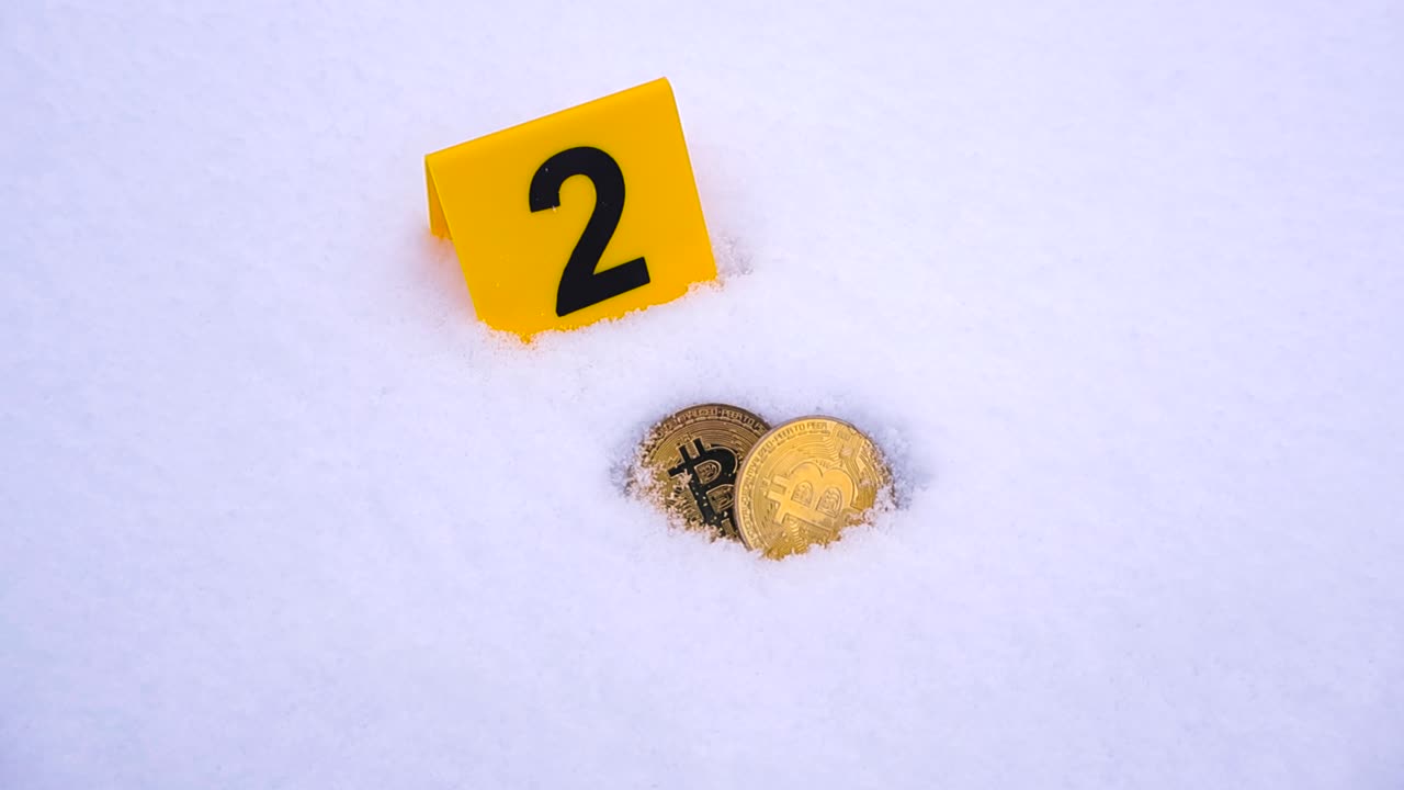 Yellow colored crime scene sciene police marker next to golden shiny bitcoin cryptocurrency coins that are in white fluffy and soft winter snow. Close up video moves closer to the scene