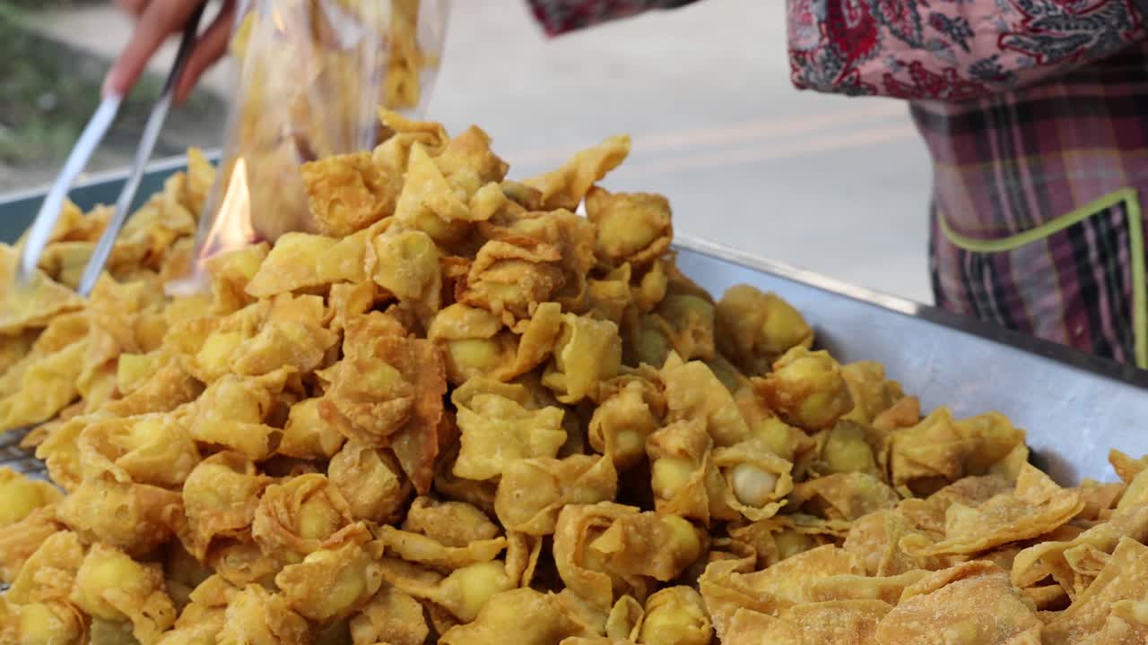 Street vendor uses tongs to bag crispy fried wontons at outdoor market in natural daylight