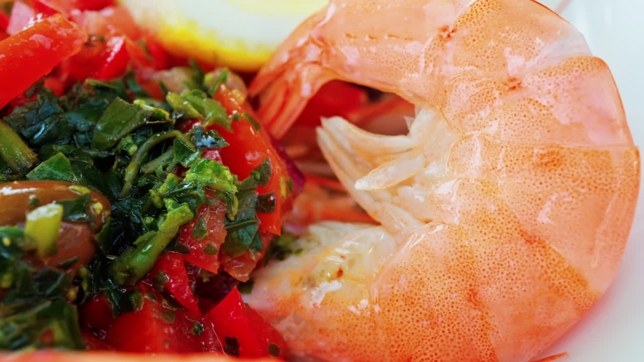 Close up of cooked shrimp with a slice of lemon and herbs on a white plate at a restaurant