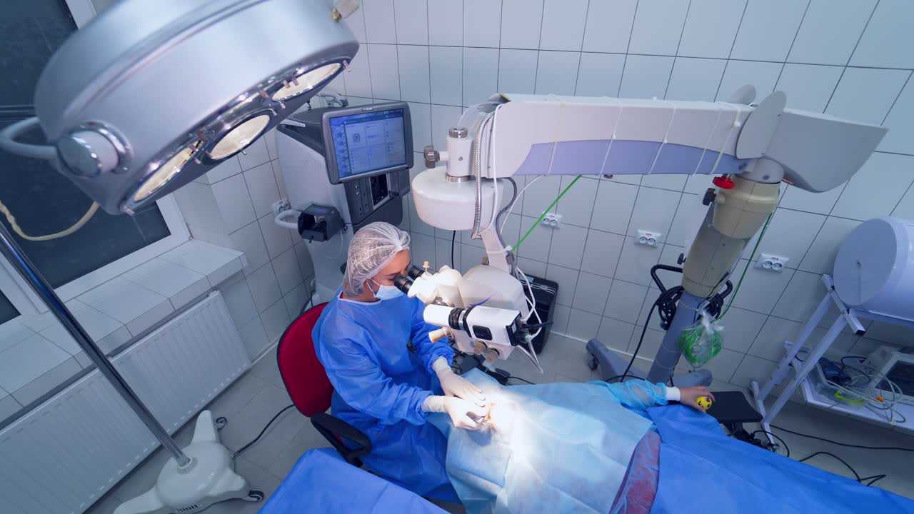 Female surgeon performs the operation on eyes in gloves and mask with microscope. Ophthalmologist treats patient's eyes in a modern clinic.
