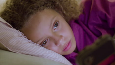 closeup of mixed race girl lying in bed, using her mobile phone