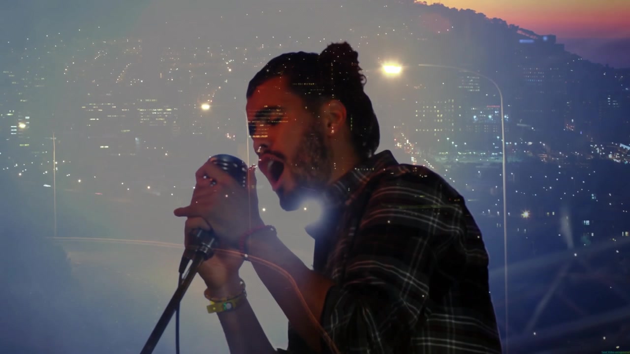Male singer humming into mic stand, intensifying vocals as city lights pulsing around silhouette