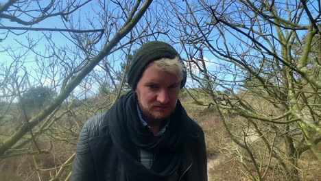 toma en cámara lenta extrema de un auténtico hipster con barba caminando por el bosque mientras mira directamente a la cámara