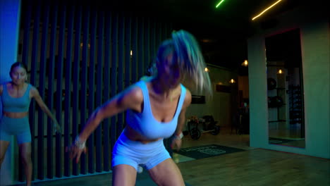 cámara lenta de una entrenadora mexicana latina morena con cola de caballo enseñando a sus estudiantes cómo hacer burpees y mirando a la cámara