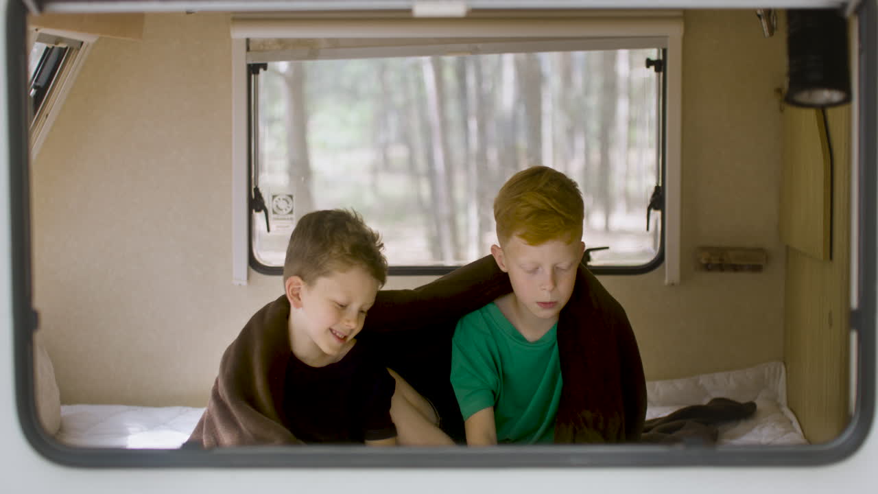 캠퍼밴의 침대에 앉아 책을 읽고 있는 두 남동생