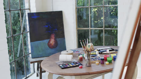 close up of paintings on easels and paints and brushes on table in studio, slow motion