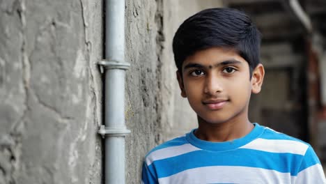 confident indian boy wearing a striped t shirt leans against a weathered wall in an urban environment, his calm expression reflecting resilience and hope