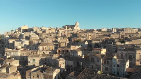 flying low over barogue city modica during sunrise and blue sky, aerial