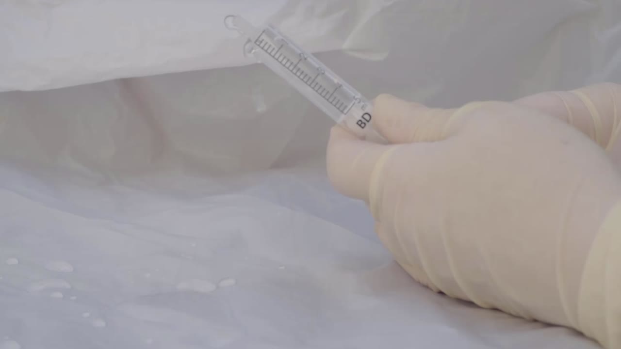 Hand wearing medical gloves holding plastic medical syringe squirting water