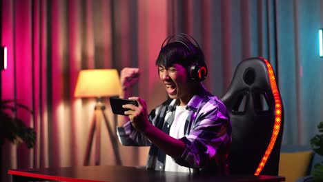 excited asian teen boy gamer celebrates victory and dancing while playing video game on smartphone