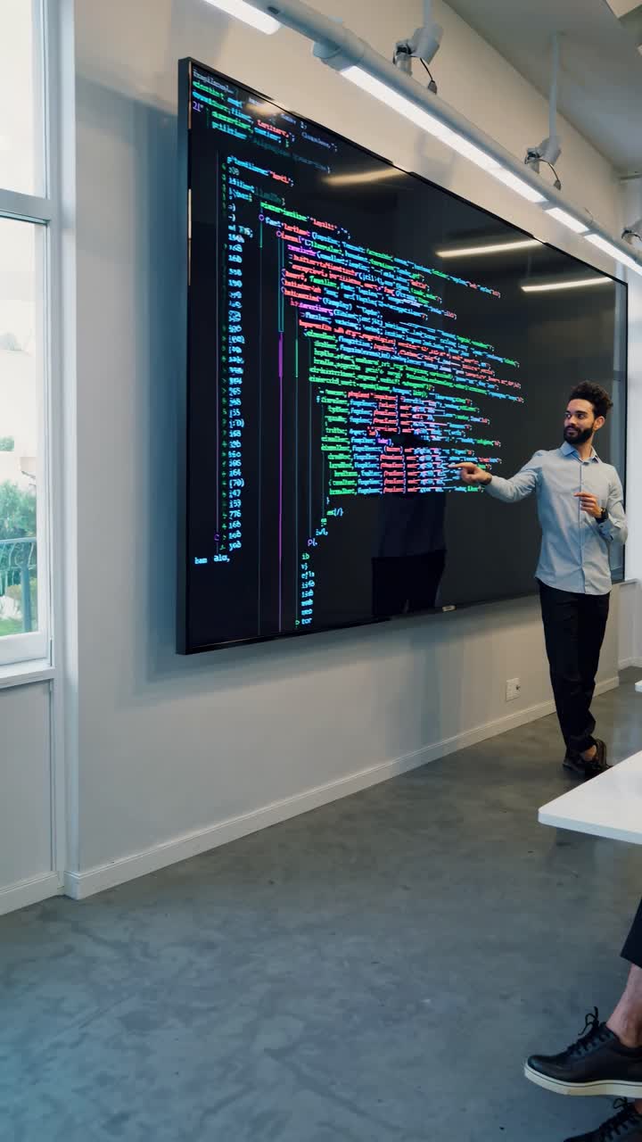A man presents colorful code on a large screen in a modern office