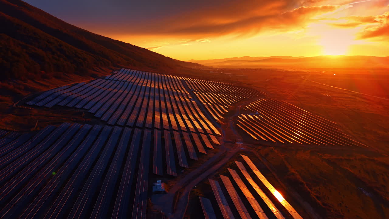 Solcelleparkens infrastruktur i gyldent solnedgangslys med bjerge. En storstilet installation for vedvarende energi ved skumringstid med lange skygger og sol.