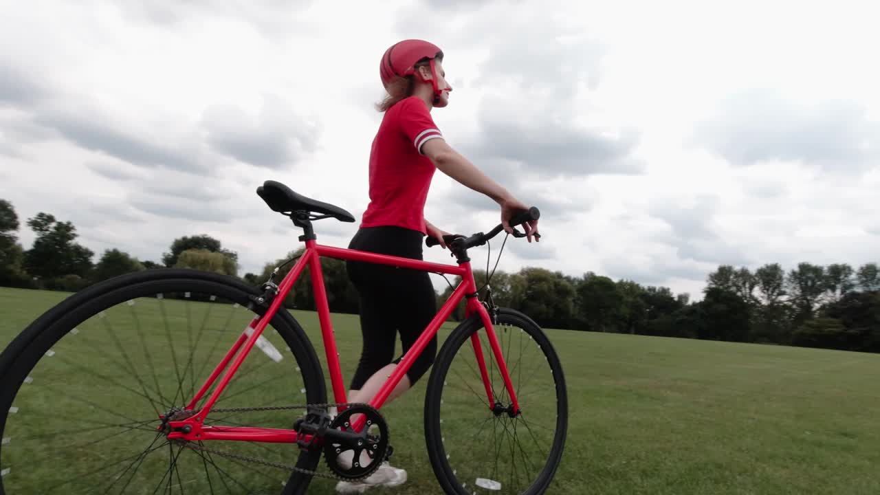 Ciclista caucásica con top rojo caminando con su bicicleta en un parque