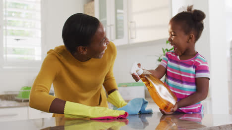 african american mother and daughter cleaning countertops and laughing in kitchen