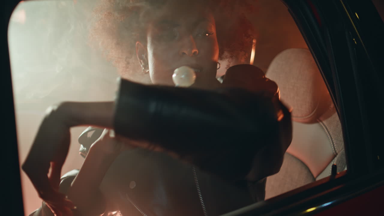 Carefree girl licking lollipop sitting car backseat in night neon glow closeup