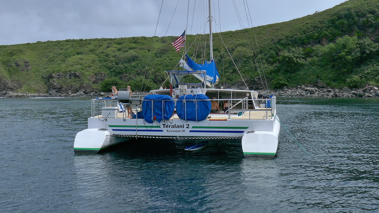 Two girls grilling out and waving on the back of Teralani two in Honolua Bay, Maui Hawaii