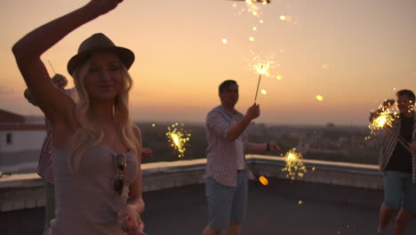 Young-females-on-the-roof-move-a-dance-with-their-boyfriends-on-a-summer-evening-with-big-bengal-light.-It's-a-pleasure-sunset-before-night.-Their-hair-blows-beautifully-in-the-wind.