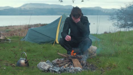 Camping-young-man-puts-kettle-on-fire-camping-by-lake-4K