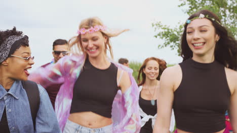 group of excited young friends carrying camping equipment through field to music festival