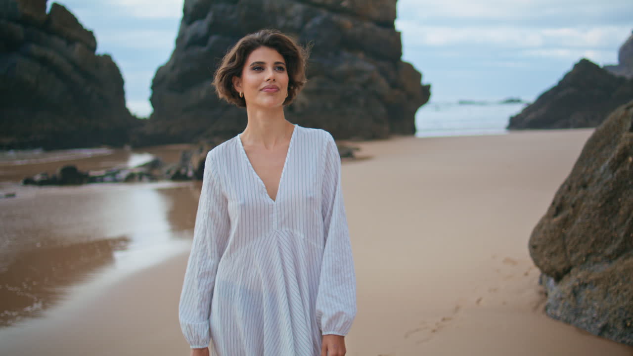 una mujer romántica admirando la playa en una isla rocosa. una mujer sonriente caminando por la costa arenosa.