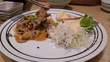 eating a serving of spicy stir-fried meat with chilies and garlic using chopsticks, with vegetable salad as a side dish