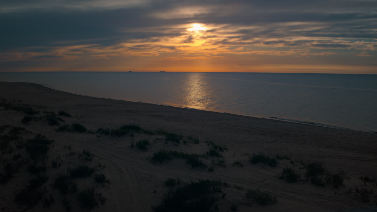 Widok z drona na plażę z małymi zielonymi krzewami na tle jasnego pomarańczowego zachodu słońca.