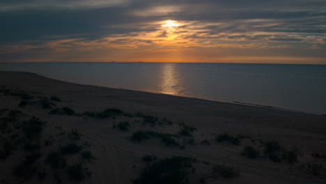 vista de la playa de aviones no tripulados con pequeños arbustos verdes contra un atardecer naranja brillante.
