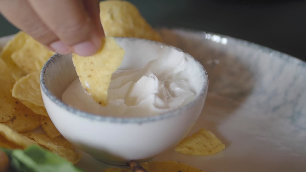 Hand dipping tortilla chip in a bowl of creamy sauce