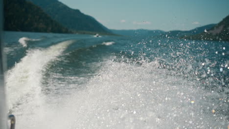 surface of water foams from fast movement of high-speed yacht. trace of motor boat on water surface on warm day. splashes rise high shining in sunlight slow motion