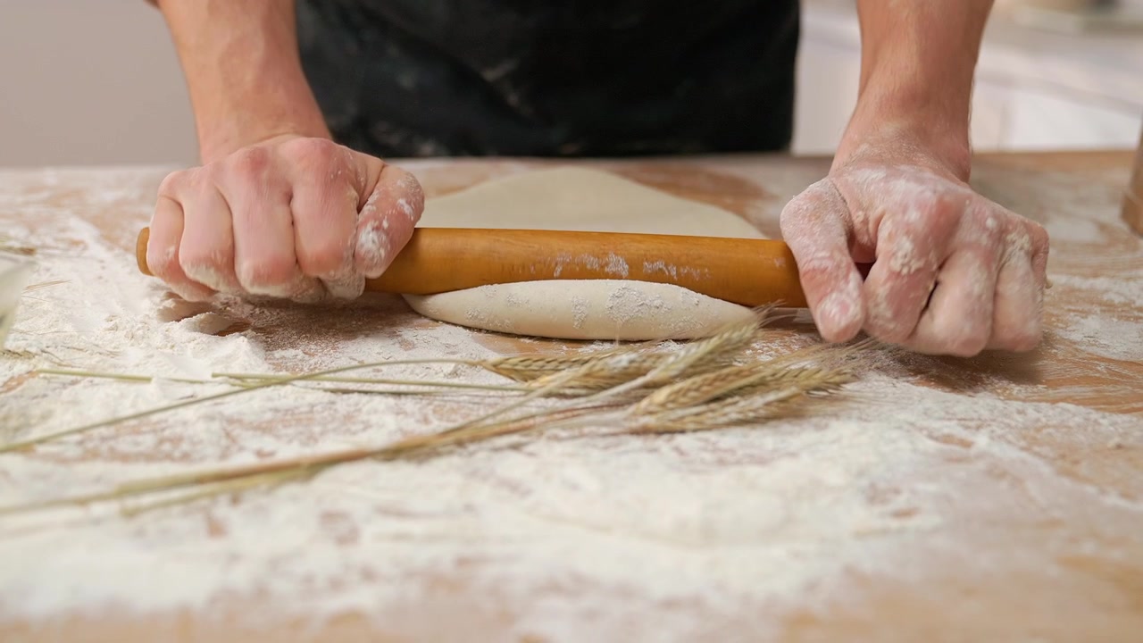 Close-up of Hands Rolling Dough with a Wooden Pin on a Floured Table