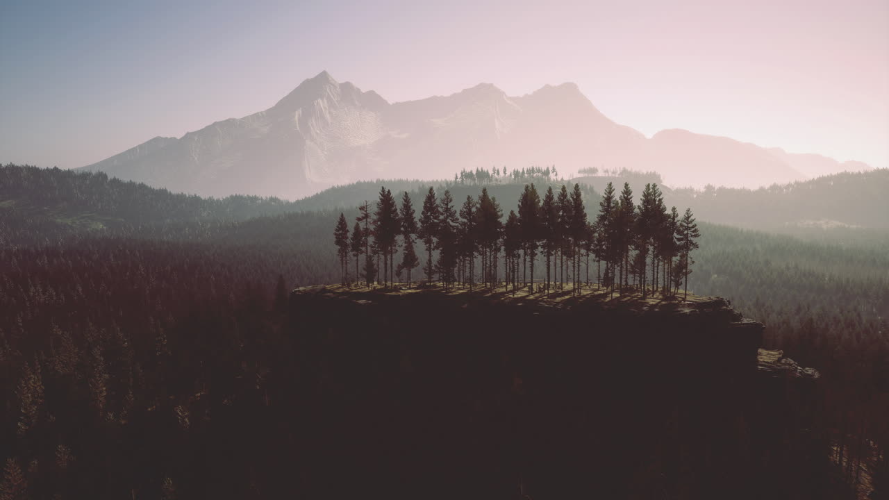Mountains cradle a solitary forest atop a rocky cliff at sunset