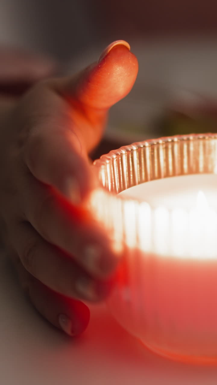 여성의 손은 스타일리시한 유리 개에 불타는 불을 돌리고, 반 어두운 방에서 축제 저녁 식사 중에 테이블에 앉아 극심한 클로즈업 느린 동작